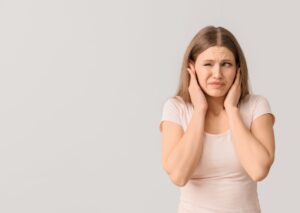 Woman in light pink shirt holding her head with both hands, displaying discomfort or distress from indoor air or temperature issues.