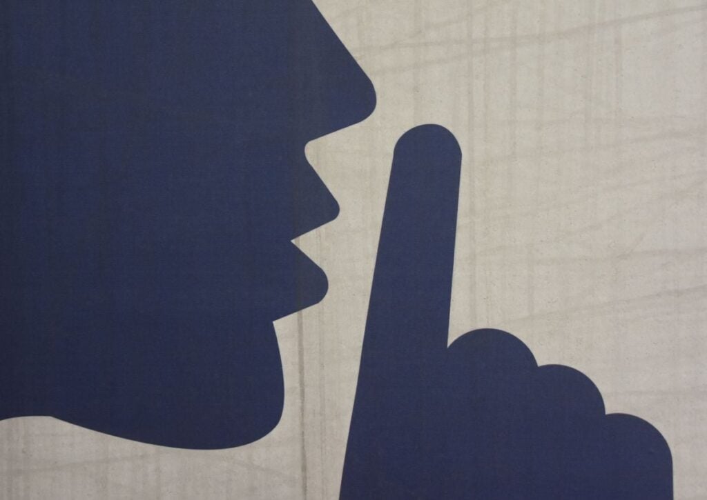 Silhouette illustration showing a person's profile with a finger raised to lips in a shushing gesture, representing quiet HVAC operation.