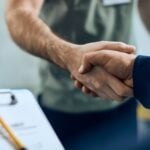 Two people shaking hands over a document, symbolizing a business agreement or service contract for HVAC, plumbing, or electrical work.